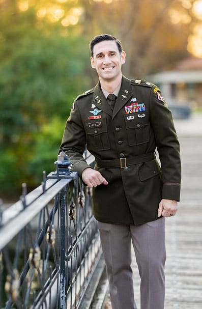 Nick Barringer, Human Performance Consultant and Nutritional Physiologist, stands outside on a historic bridge, decorated in Army uniform